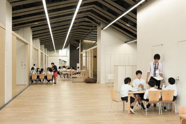 Interior of school, showing the open seating areas and enclosed school rooms under a long, continuous roof. Image via Kengo Kuma and Associates.